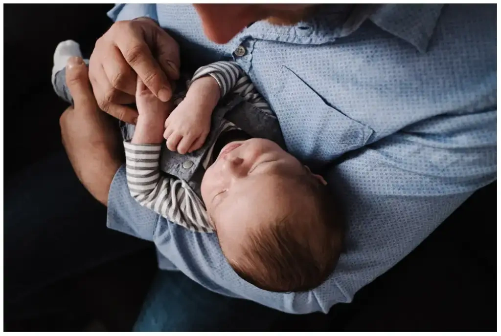 Père tenant son nouveau-né endormi dans ses bras pendant une séance photo de naissance.