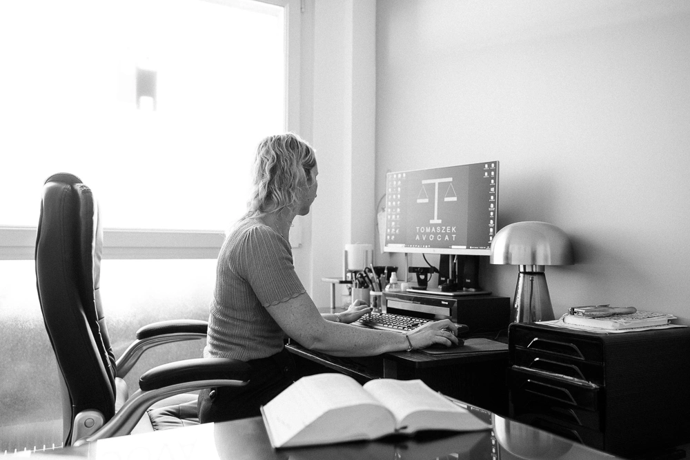 Femme travaillant sur un ordinateur dans un bureau lumineux photographié en noir et blanc.