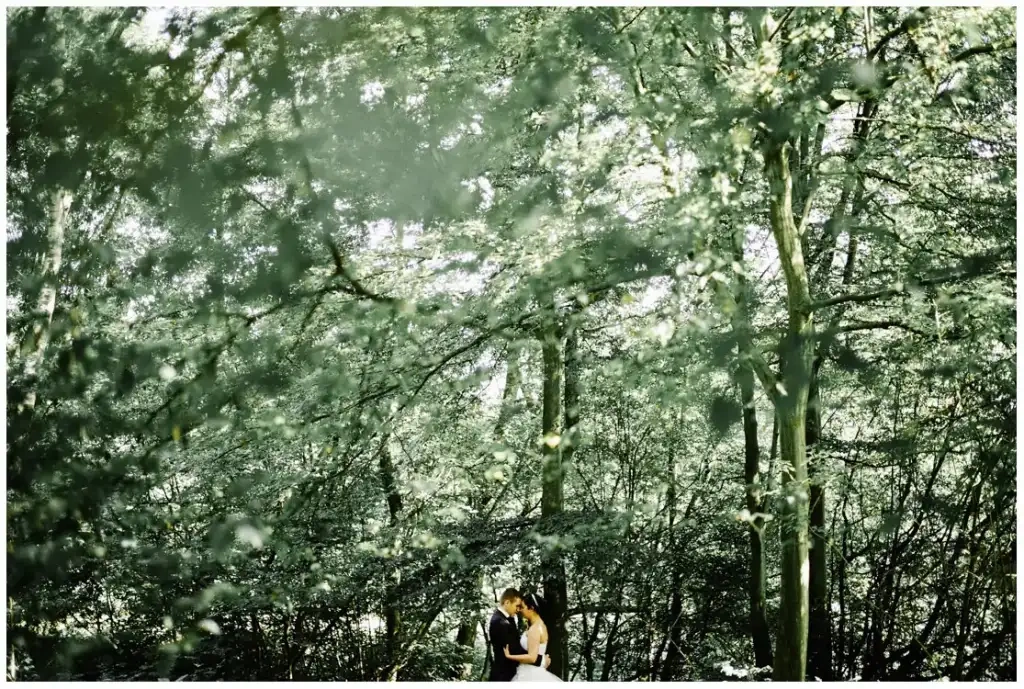 Couple s'embrassant sous de grands arbres lors d'une séance photo en forêt.