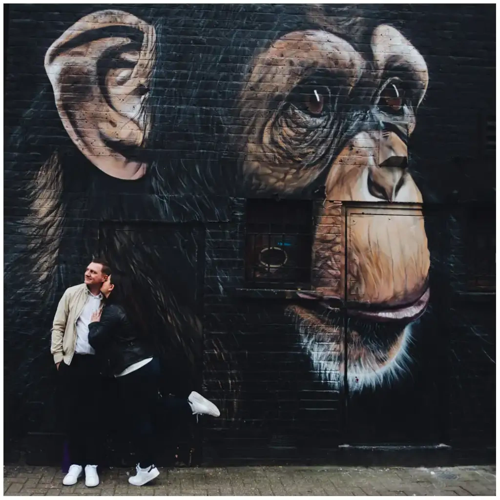 Couple posé au pied d'une grande fresque urbaine représentant un chimpanzé.