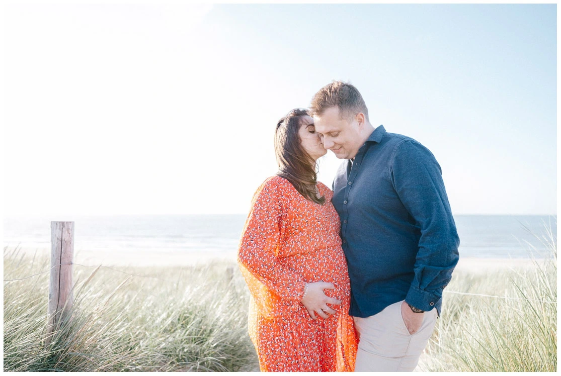 Couple enlacé devant la mer lors d'une séance photo de grossesse lumineuse.