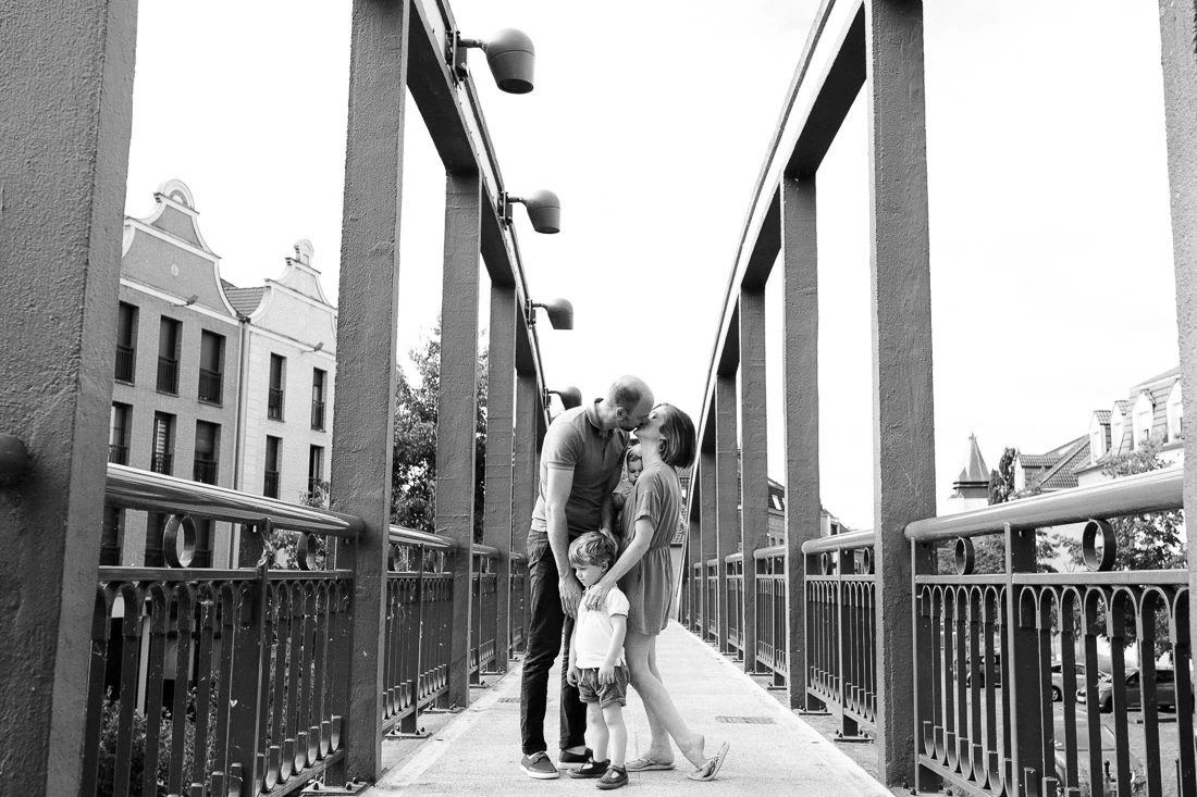 Couple s’embrassant au-dessus de son jeune enfant sur une passerelle lors d’une séance photo de famille.
