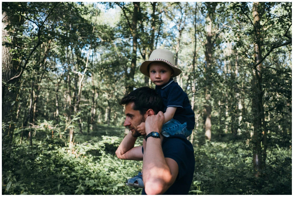Père portant son jeune enfant sur ses épaules pendant une promenade en forêt.