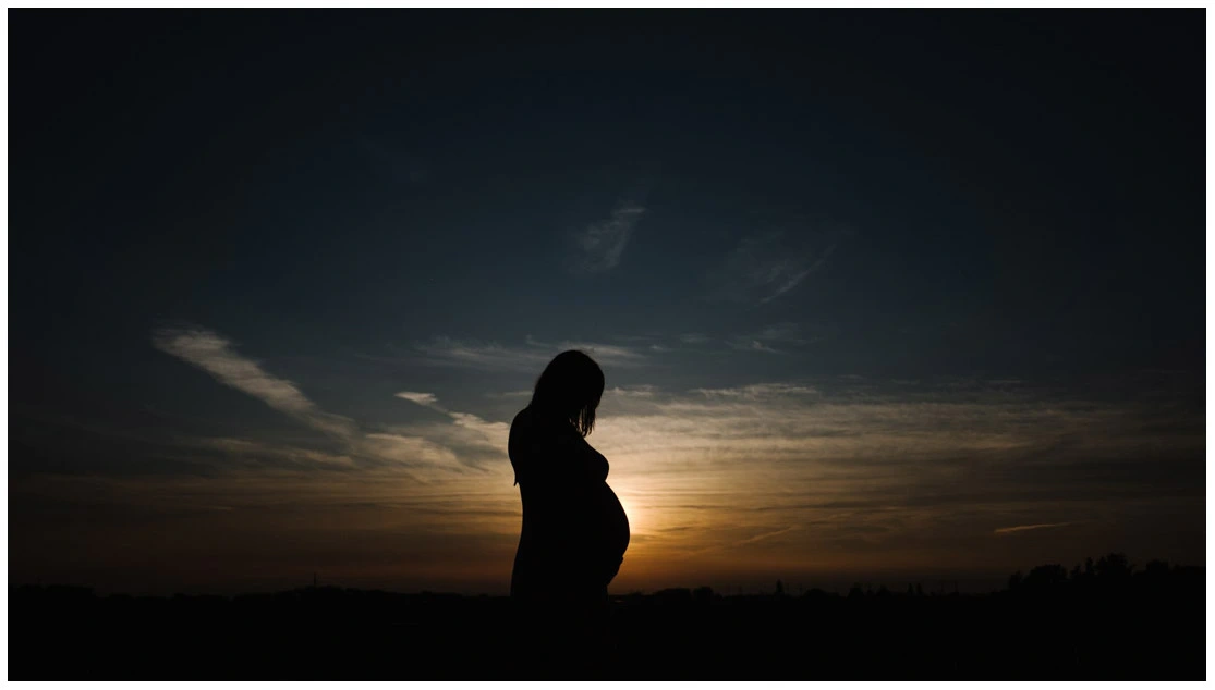 Silhouette d’une femme enceinte de profil devant un coucher de soleil.