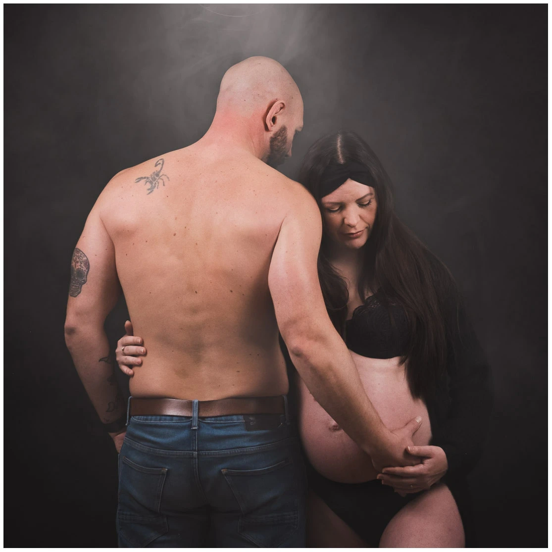 Couple entourant de ses mains le ventre de la future mère pendant une séance photo de grossesse intimiste.
