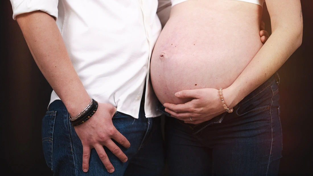 Gros plan sur le ventre d'une femme enceinte aux côtés de son partenaire pendant une séance photo de grossesse.