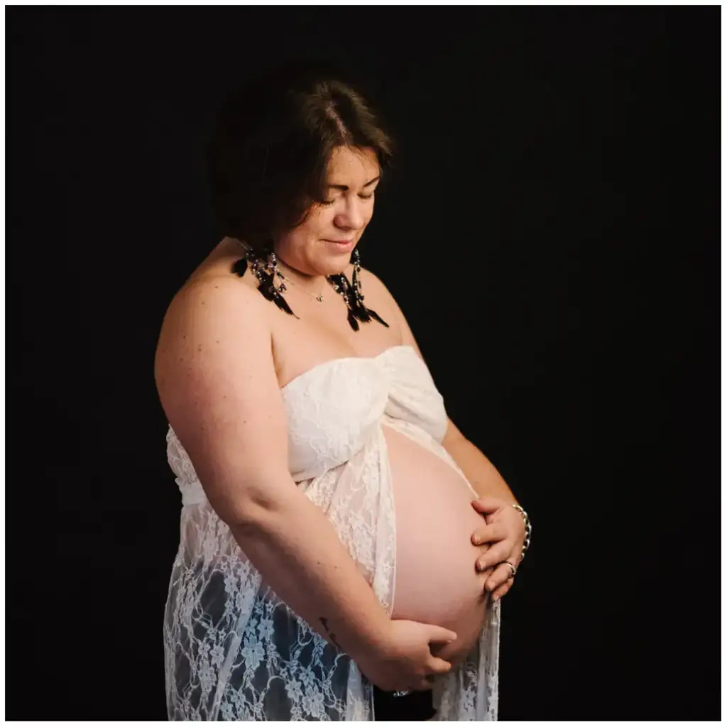 Femme enceinte en dentelle blanche tenant son ventre pendant une séance photo de grossesse.