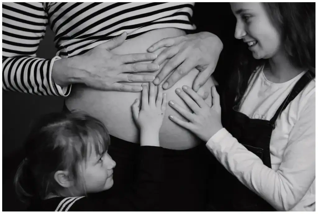 Deux enfants posant leurs mains sur le ventre d'une femme enceinte pendant une séance photo de grossesse en noir et blanc.
