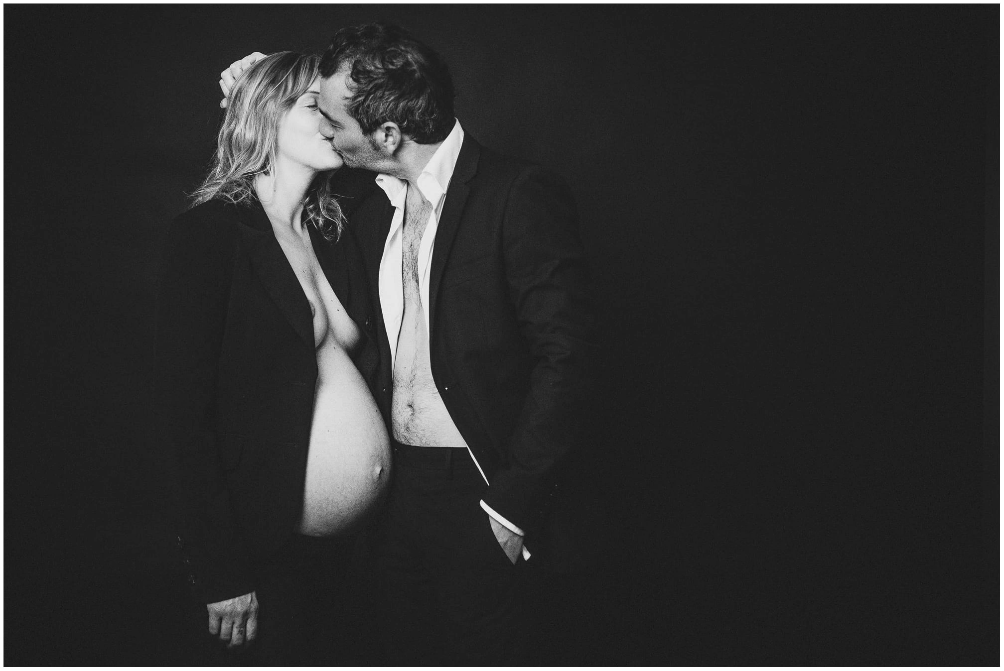 Couple tenant une échographie devant le ventre de la future mère pendant une séance photo de grossesse en noir et blanc.