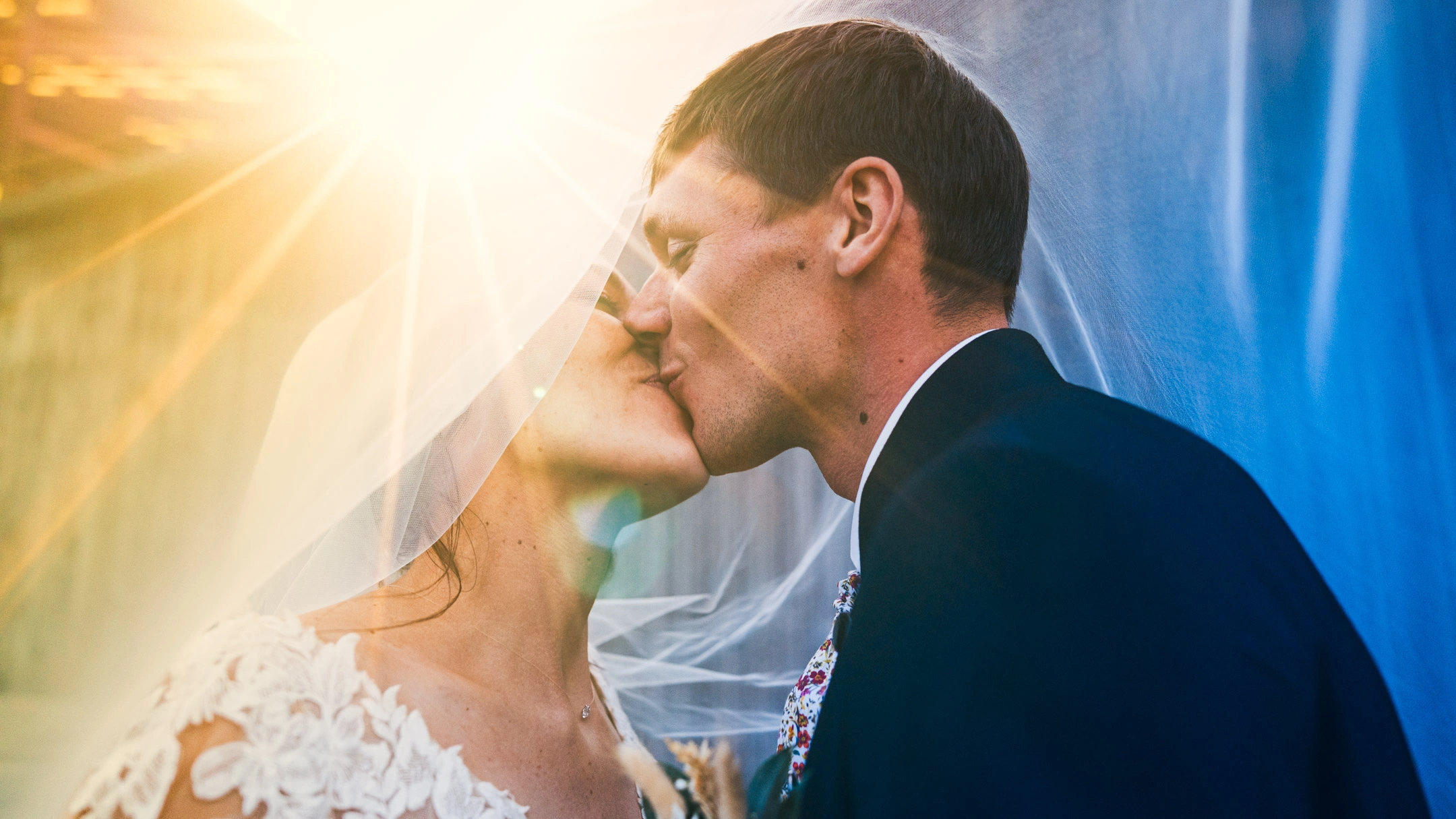 Léa et Charles s'embrassant sous le voile de la mariée dans une lumière dorée.