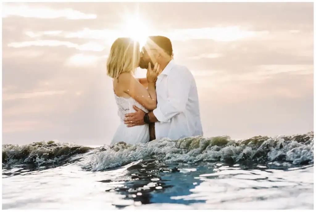 Mariés s'embrassant dans la mer au coucher du soleil pendant leur reportage photo de mariage.