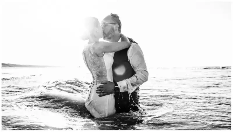 Mariés s'embrassant dans la mer lors d'un reportage photo de mariage en noir et blanc.