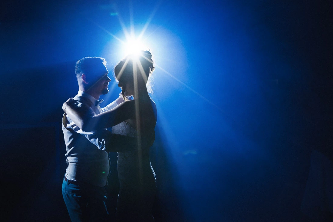 Mariés enlacés pendant leur danse sous un projecteur bleu lors d'un reportage de mariage.