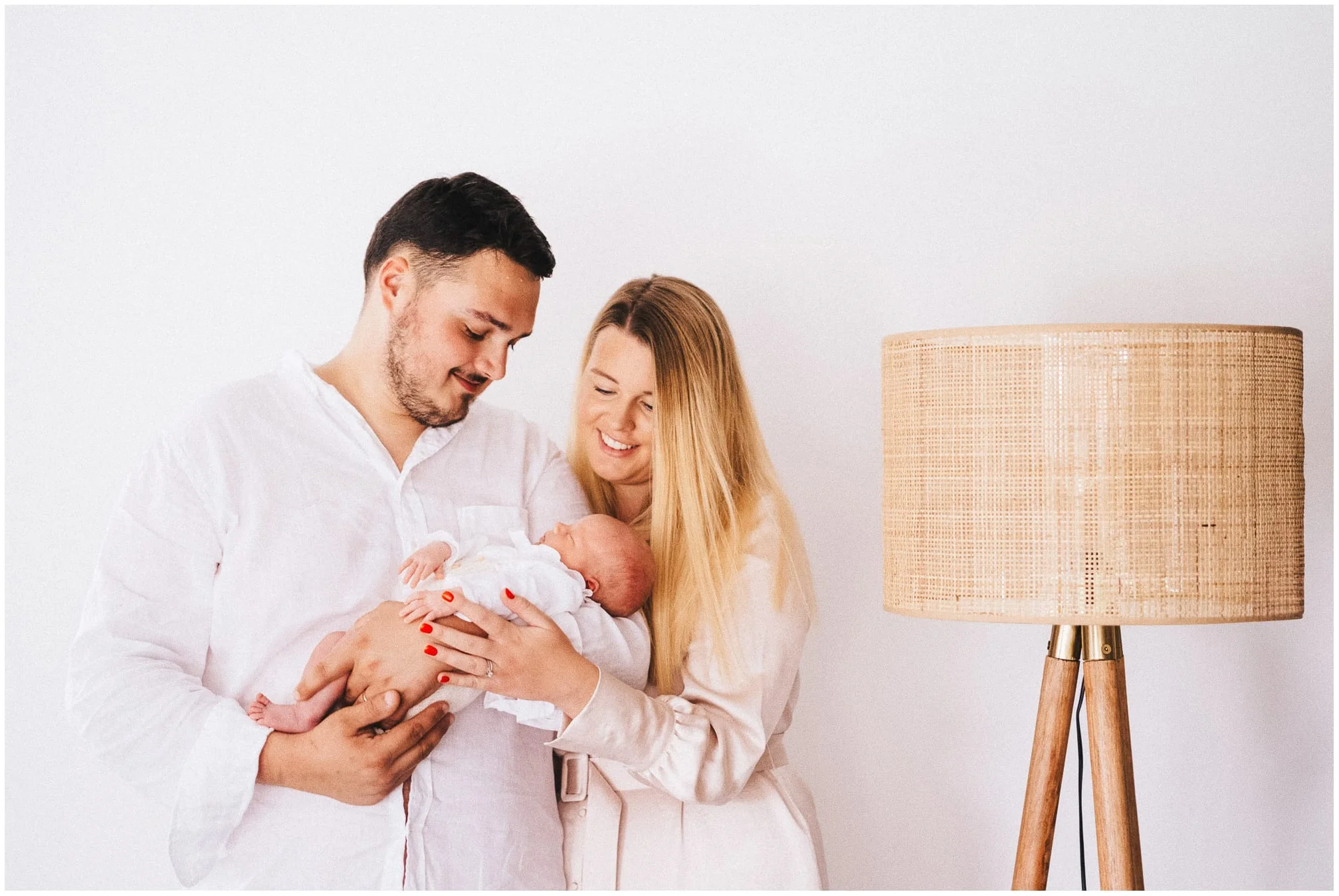 Parents souriants tenant leur nouveau-né pendant une séance photo de naissance dans un intérieur lumineux.