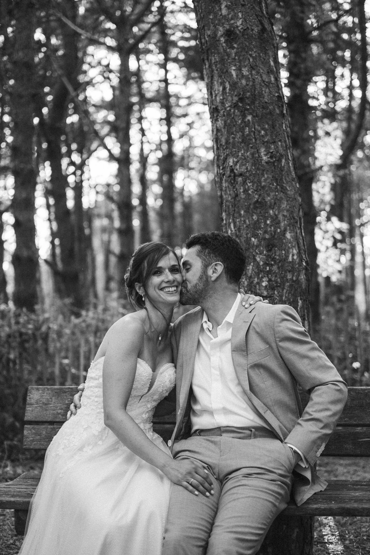 Anthony embrassant Caroline sur la joue alors qu’ils sont assis sur un banc en forêt, en noir et blanc.