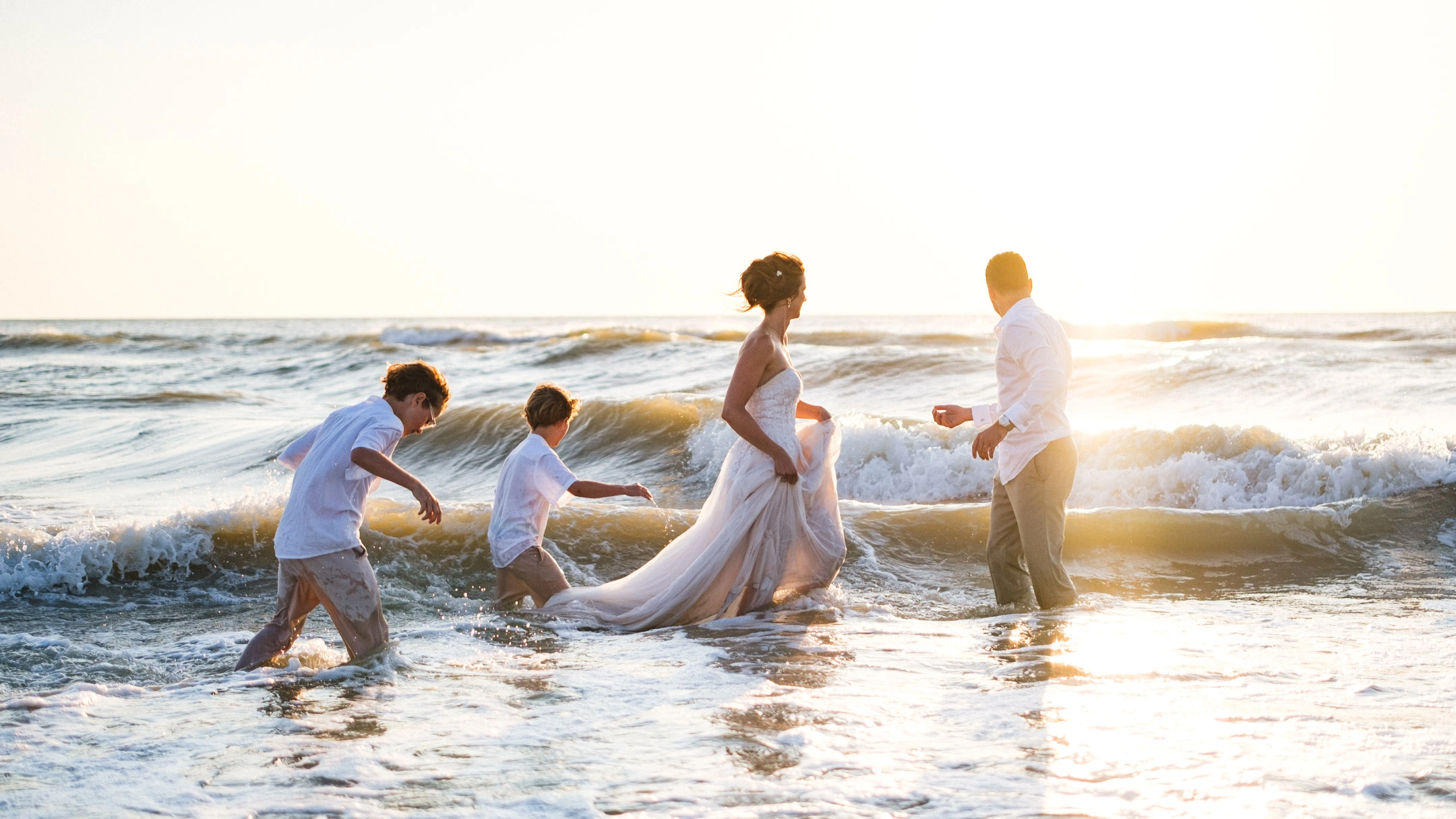 Caroline et Anthony dans les vagues avec leurs deux enfants au soleil couchant.