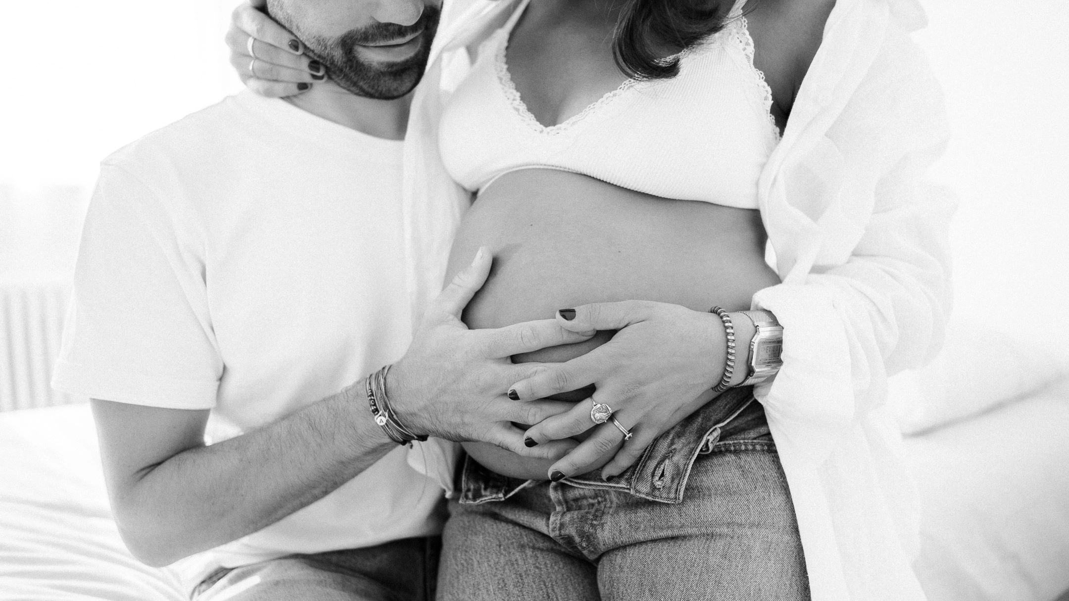 Les mains d'un couple réunies sur un ventre de grossesse dans un portrait en noir et blanc.