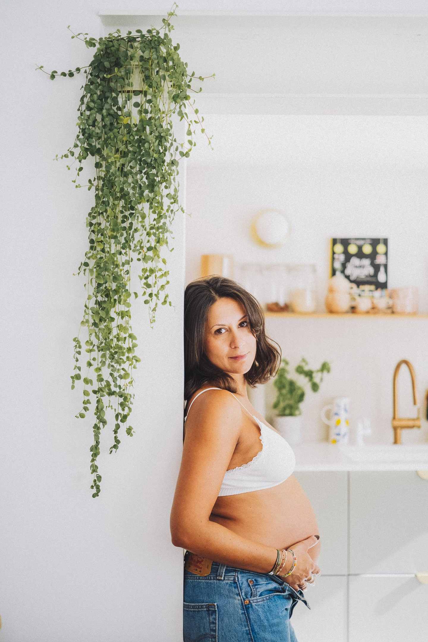 Portrait d'une future maman debout dans sa cuisine lumineuse, les mains posées sur son ventre.