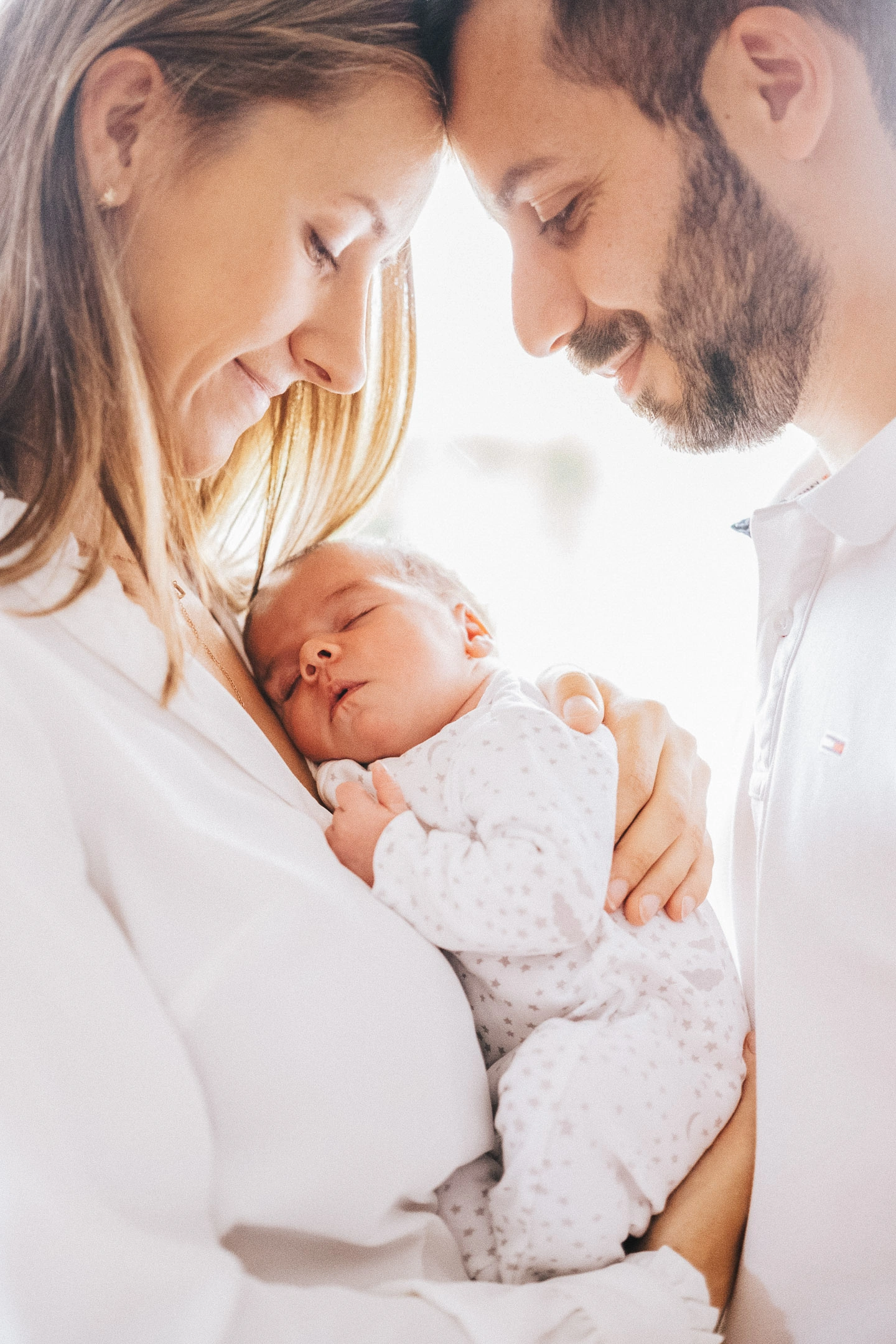 Deux parents rapprochent leurs visages au-dessus de leur nouveau-né endormi dans les bras de sa mère.