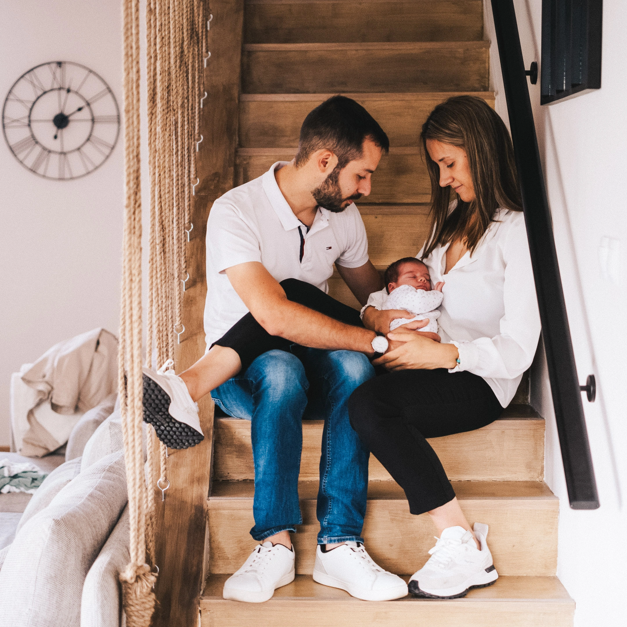 Deux parents assis dans un escalier en bois entourent leur nouveau-né endormi.