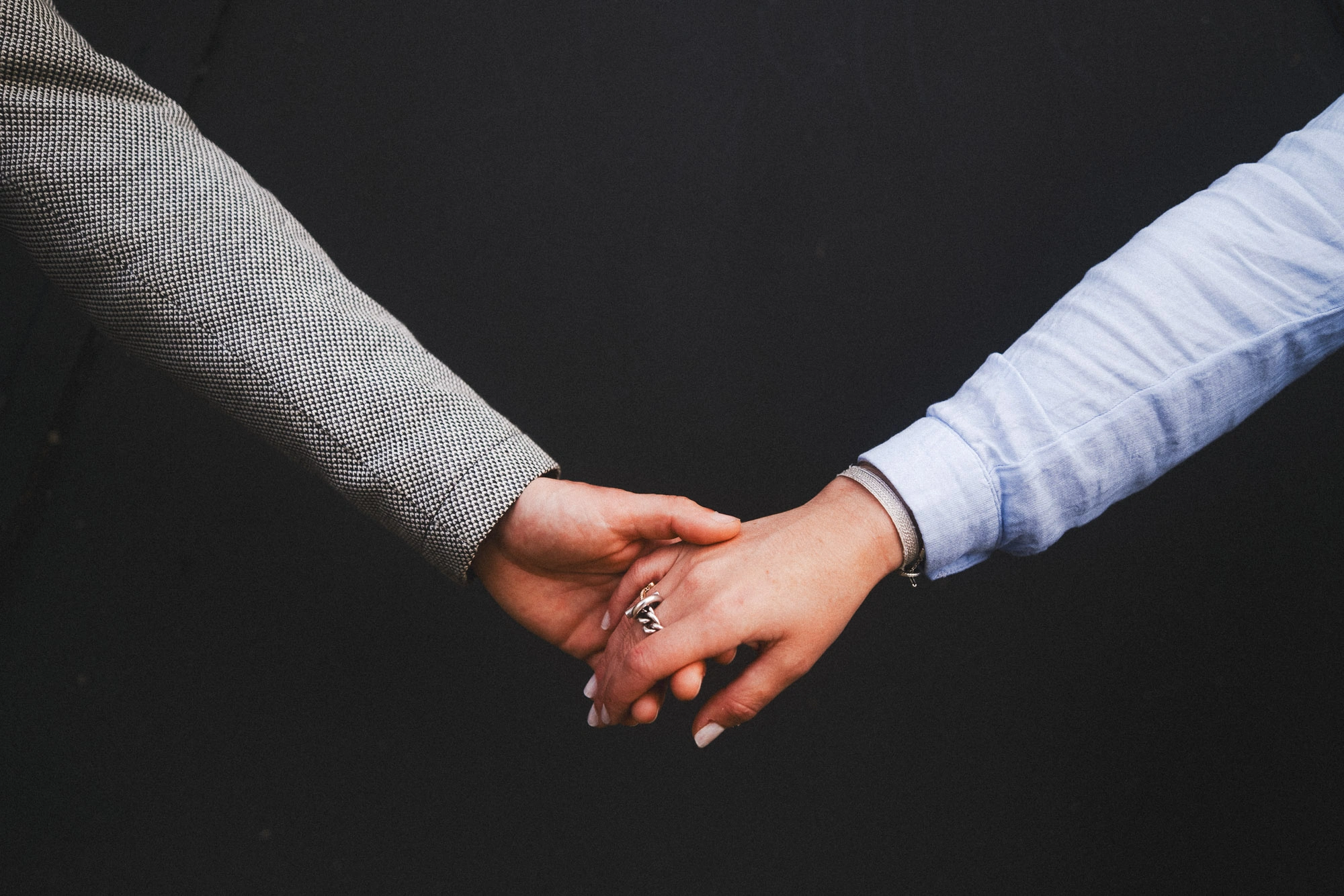 Mains d’un couple qui se rejoignent devant un arrière-plan sombre.