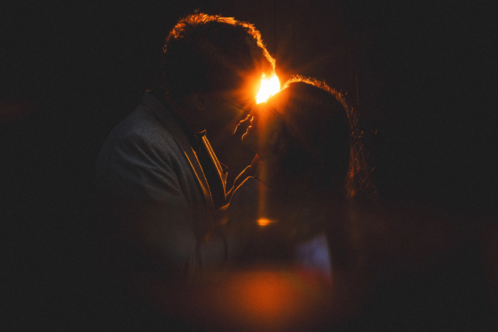 Silhouette d’un couple face à face avec une lumière orange entre leurs visages.