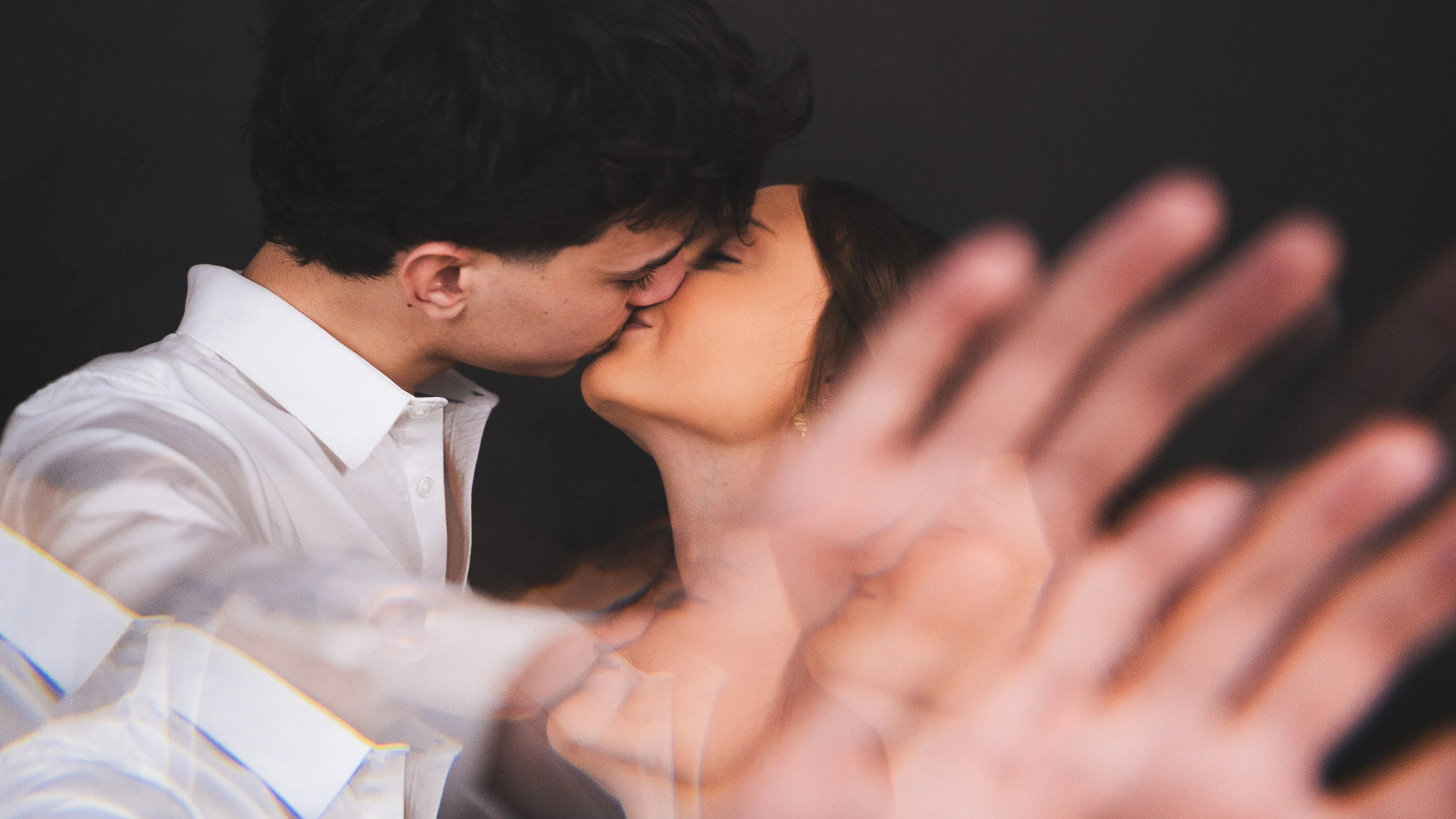 Couple s’embrassant dans une composition en double exposition avec une main floue au premier plan.