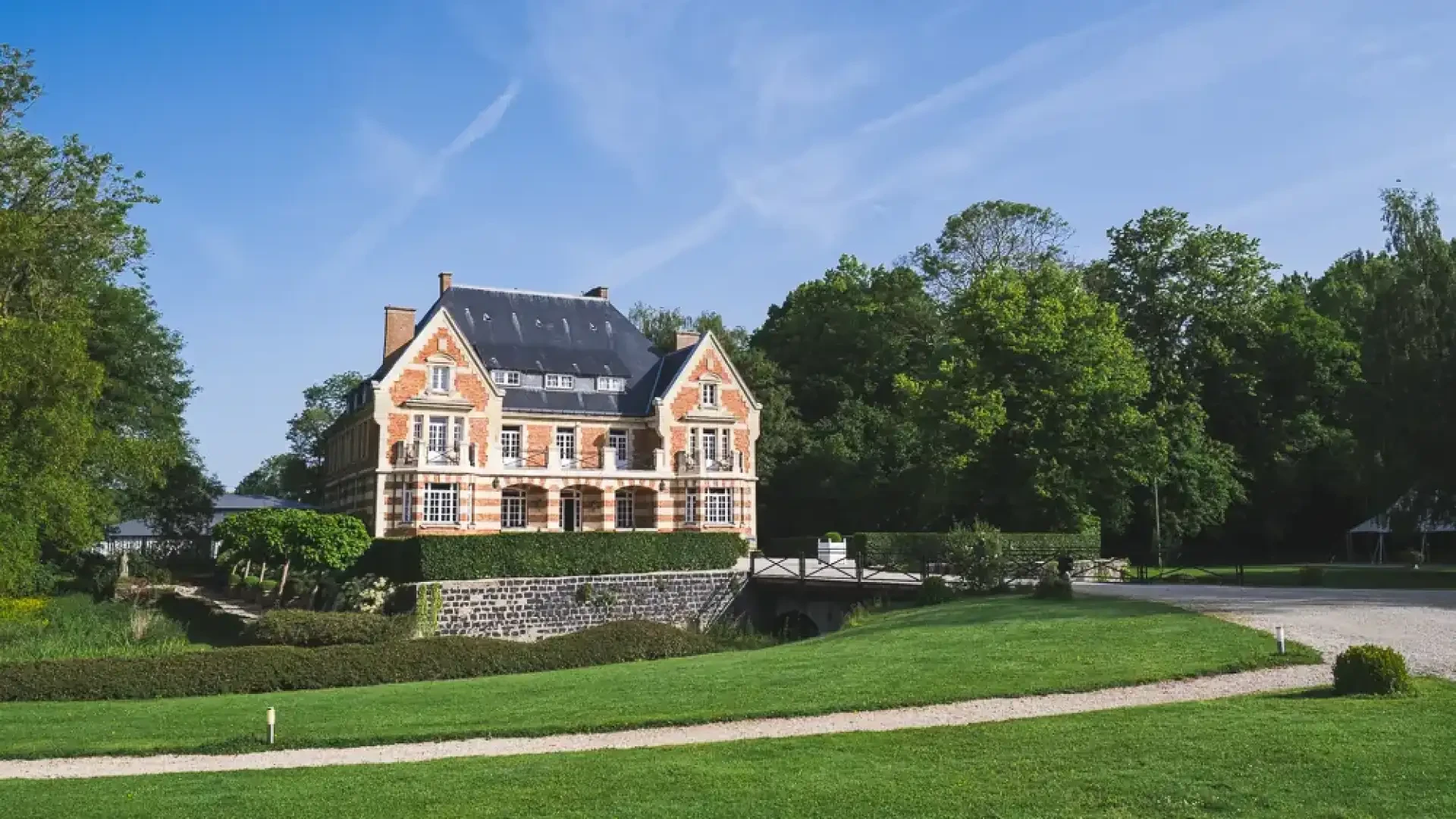 Façade du Clos Barthélemy et ses jardins sous un ciel bleu.
