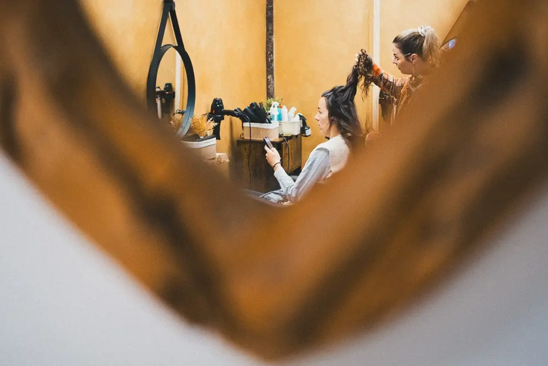 Léa observée dans un miroir pendant sa coiffure dans un salon aux tons chauds.