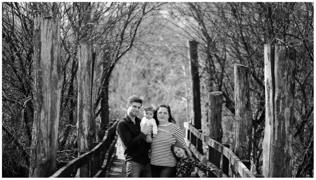 Deux parents et leurs deux enfants réunis sur une passerelle en bois, en noir et blanc.