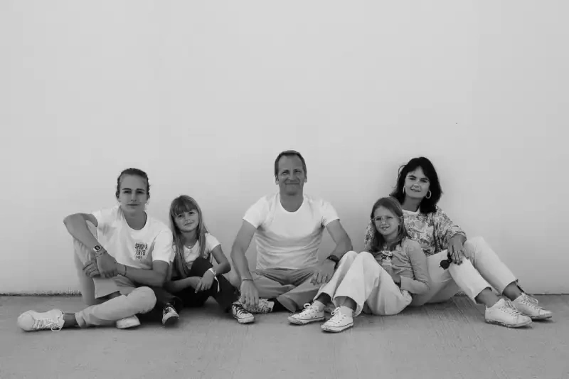 Cinq membres d’une famille assis contre un mur clair dans un portrait en noir et blanc.