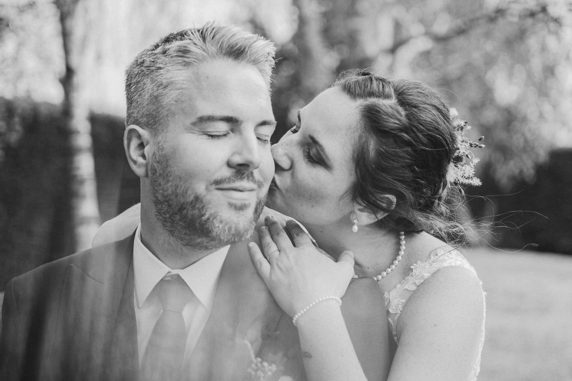 Camille embrasse Florian sur la joue, portrait de couple en noir et blanc.