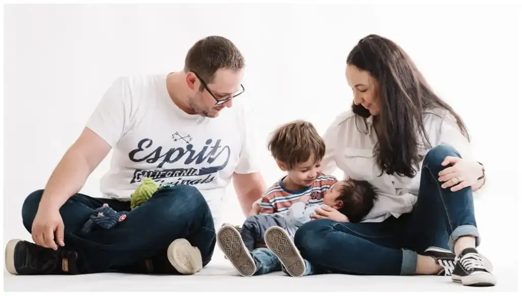 Deux parents et leur jeune garçon sont assis au sol autour du nouveau-né dans un décor blanc.