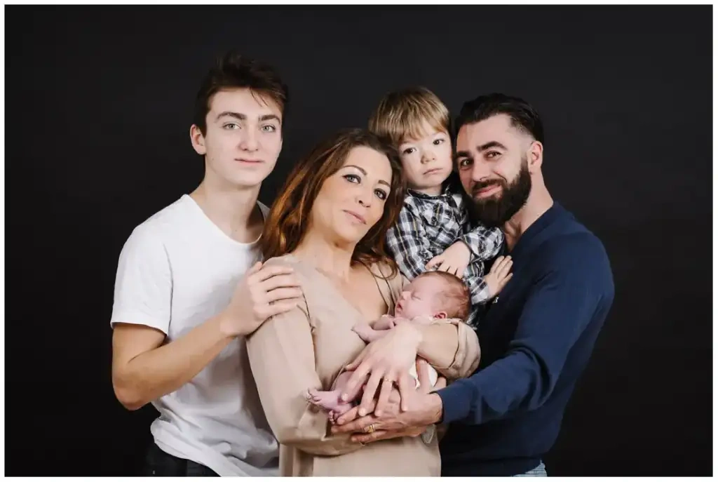 Deux parents et trois enfants entourent un nouveau-né endormi devant un fond noir.