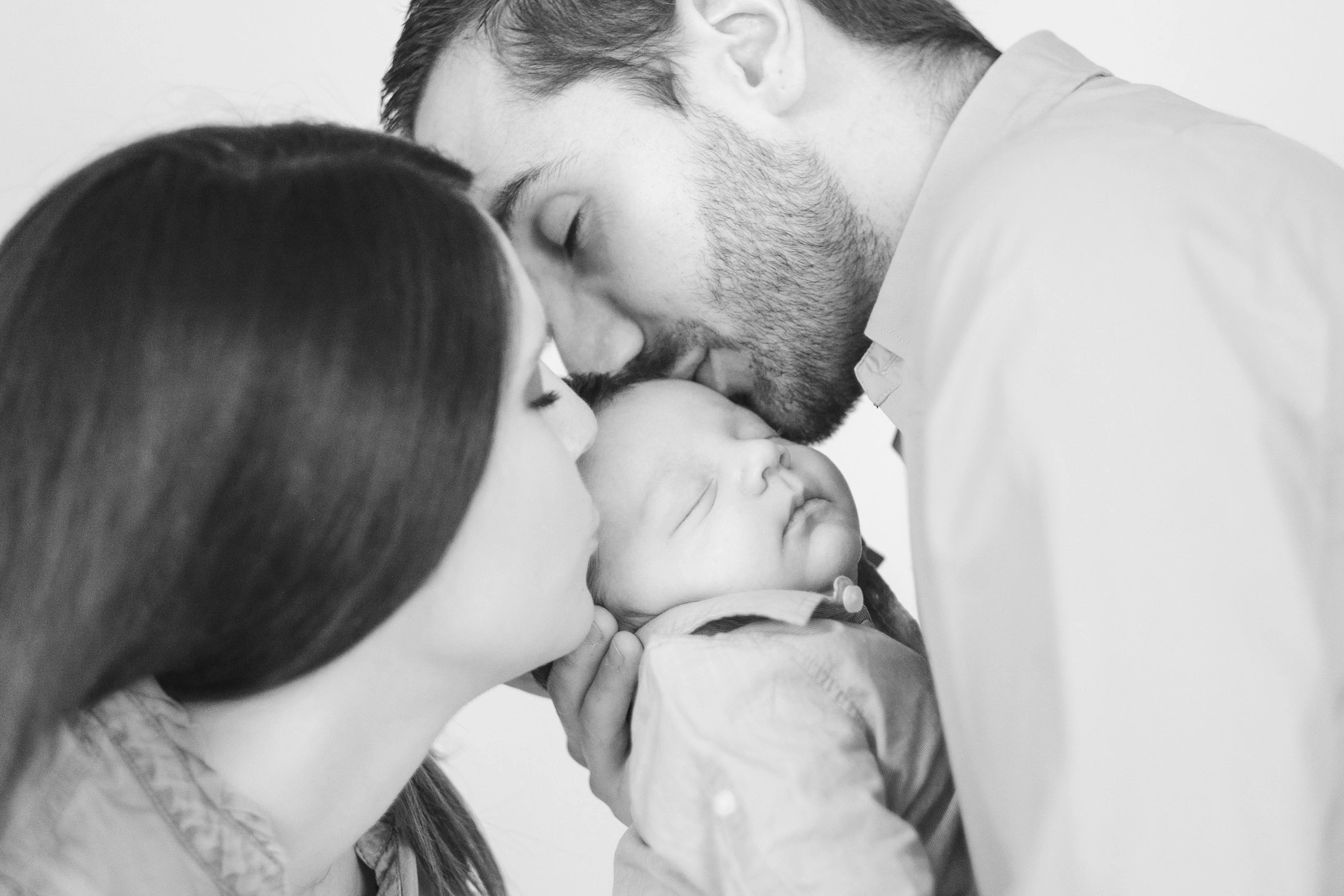 Parents embrassant leur nouveau-né endormi pendant une séance photo de naissance en noir et blanc.