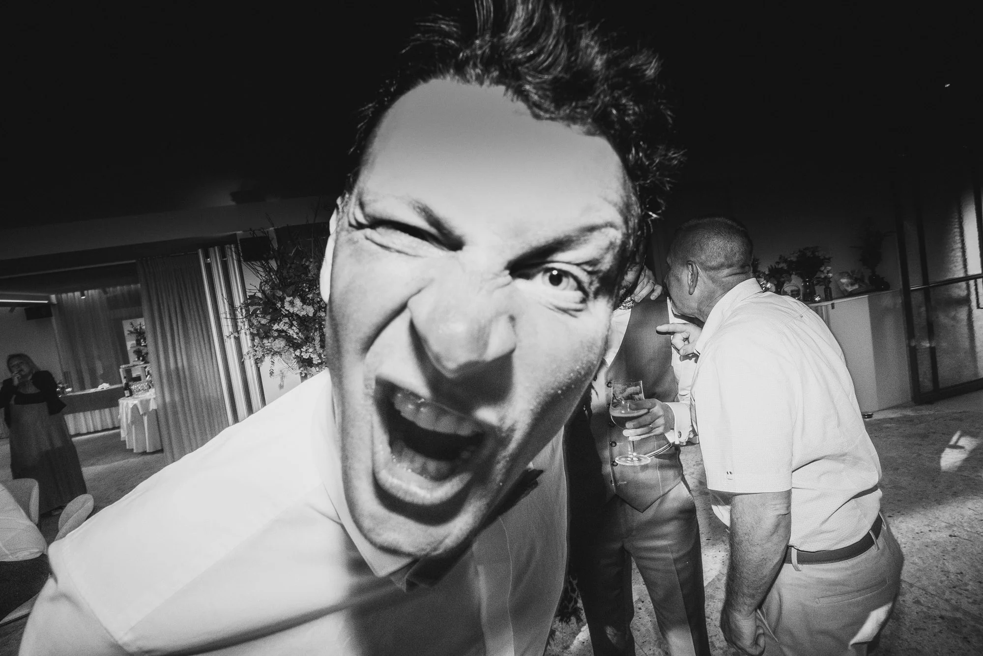 Invité faisant une grimace face à l'objectif pendant une réception de mariage en noir et blanc.