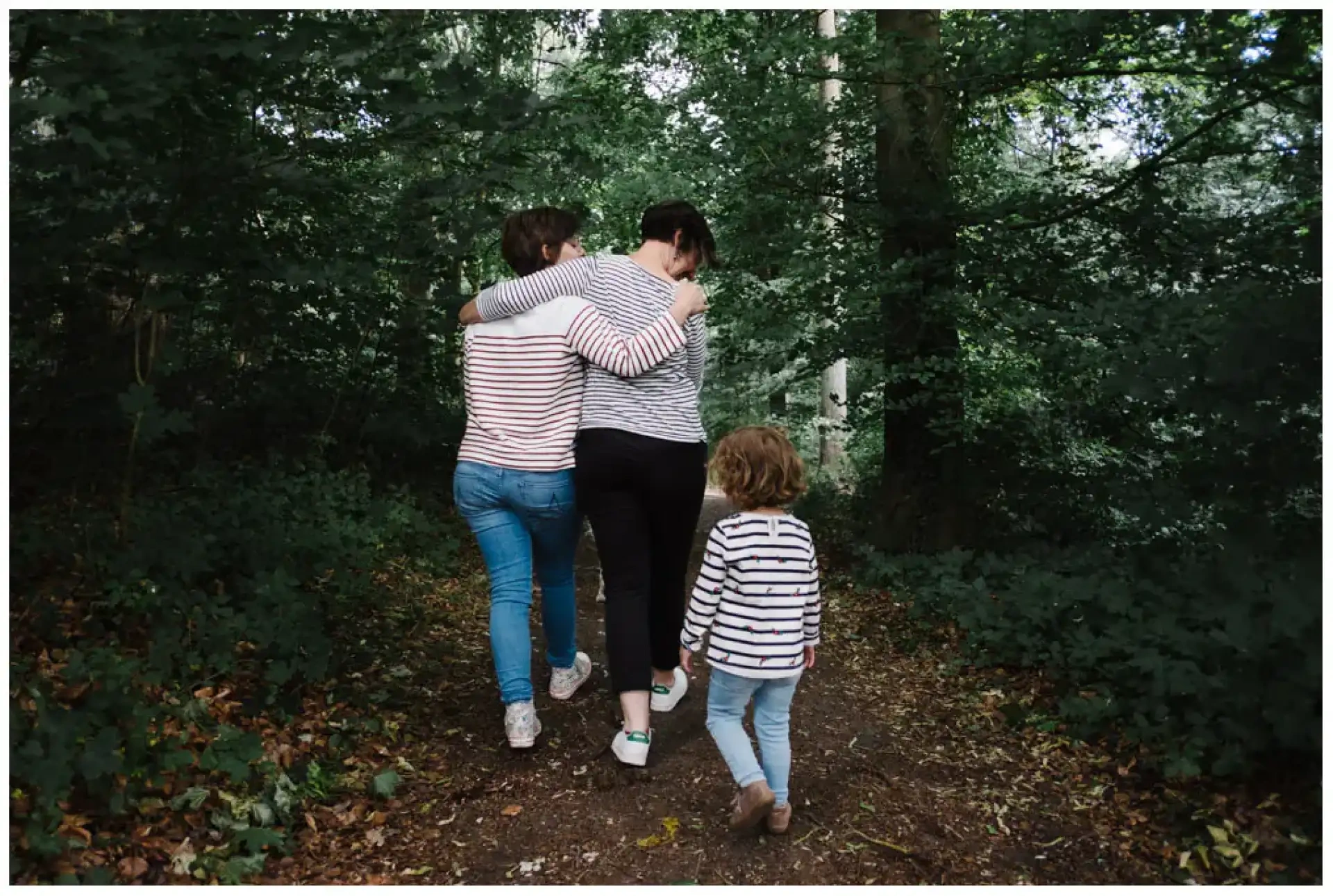 Trois personnes marchant de dos sur un chemin forestier, dont un jeune enfant.