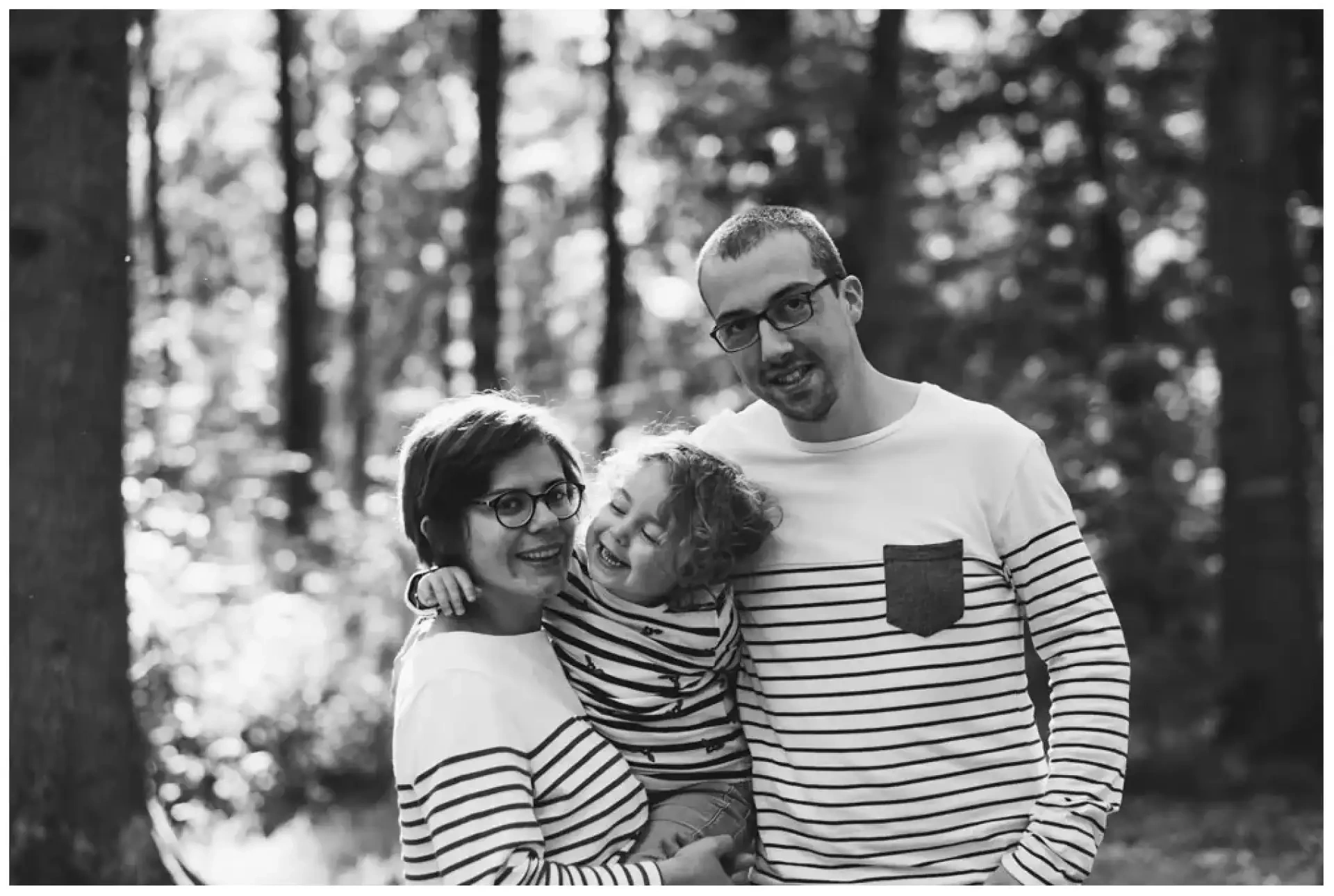 Un couple et un jeune enfant riant ensemble en noir et blanc dans une lumière en contre-jour.