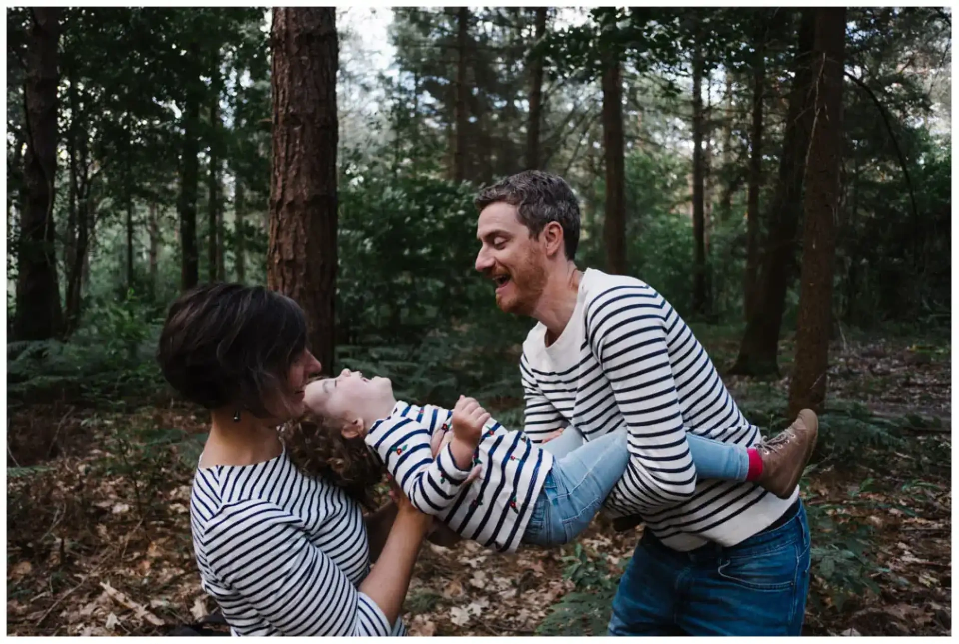 Deux adultes soulevant joyeusement un jeune enfant entre eux dans la forêt.
